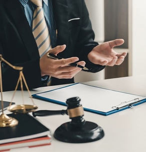 Attorney sitting at a table with a clipboard, gavel & soundblock, law books, and notebooks, explaining business law-related matters.